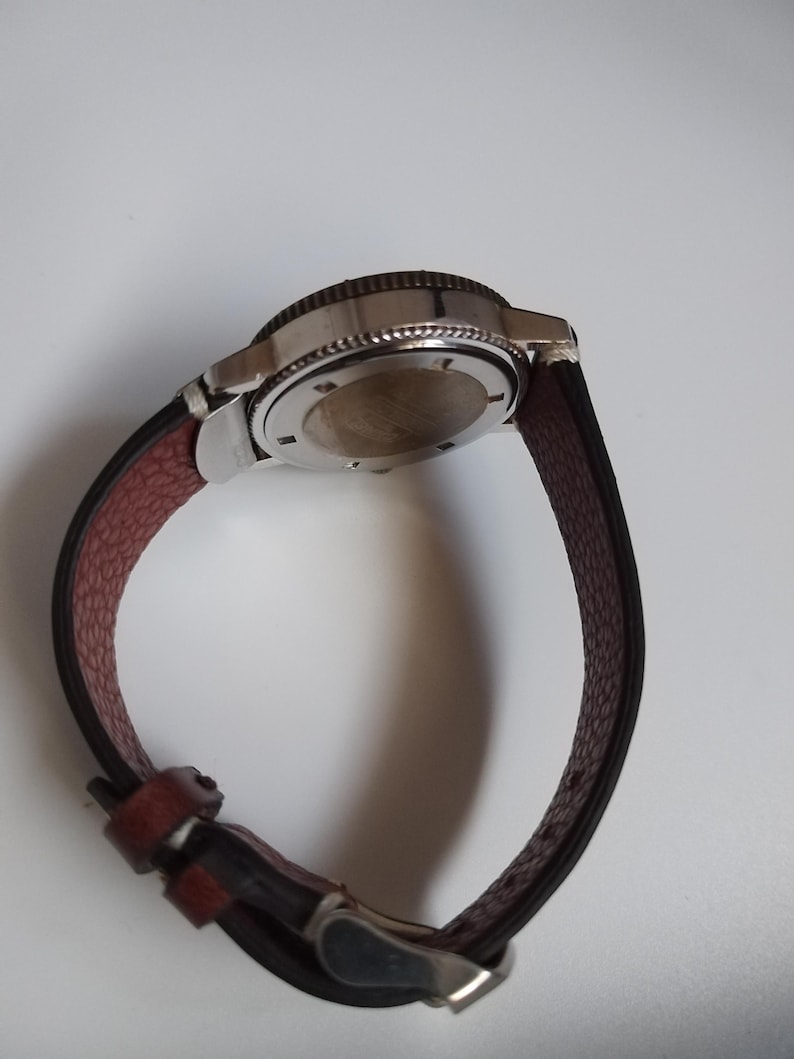 K&ouml;nnte beinhalten: Eine Armbanduhr mit einem Edelstahlgeh&auml;use und einem braunen Lederarmband. Die Uhr hat ein dunkles Zifferblatt und eine silberne Schlie&szlig;e. Das Armband ist etwa 23 cm lang.