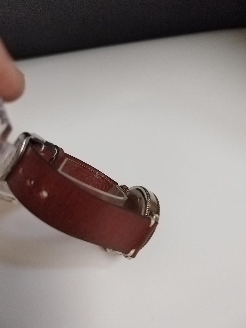 K&ouml;nnte beinhalten: Eine weinrote Uhr mit einem silberfarbenen Metallarmband. Das Zifferblatt der Uhr ist rund und hat eine strukturierte Oberfl&auml;che. Das Armband besteht aus einem glatten, festen Material.