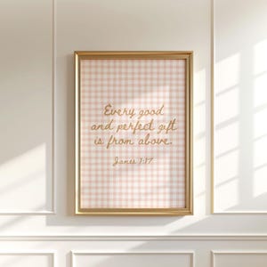Puede incluir: Una impresión de arte mural rectangular en un marco dorado con un fondo de patrón de cuadros vichy rosa claro y blanco. El texto en cursiva dorada dice: Every good and perfect gift is from above. James 1:17, centrado en la impresión.
