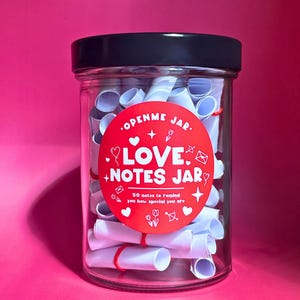 Puede incluir: Un tarro de cristal transparente con tapa negra lleno de notas blancas enrolladas. Una pegatina roja en el tarro dice "OPENME JAR. LOVE + NOTES JAR" con el texto "50 notas para recordarte lo especial que eres."