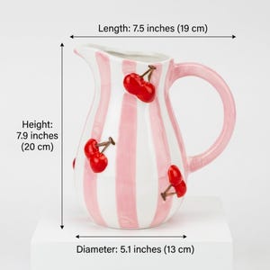 May include: A ceramic pitcher with a pink and white striped pattern, adorned with red cherry accents. The pitcher is 7.9 inches (20 cm) tall, 7.5 inches (19 cm) long, and 5.1 inches (13 cm) in diameter. It has a pink handle and a spout.