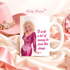 Puede incluir: Una taza de cerámica blanca con un gráfico de Dolly Parton vistiendo un vestido de lentejuelas rosa brillante. El texto en la taza dice: "It costs a lot of money to look this cheap." La taza tiene un asa estándar y un acabado liso y brillante.