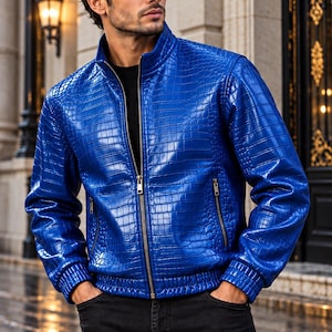 May include: A vibrant blue jacket featuring a glossy crocodile skin texture, a high collar, and a central metal zip. The garment includes long sleeves with ribbed cuffs, a ribbed hem, and two side pockets with metal zips, worn over a black shirt.