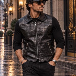 May include: A black crocodile-embossed leather vest with a front zipper closure, a pointed collar, and two zippered side pockets. The vest features side lacing details and is paired with a matching black crocodile-embossed leather baseball cap.