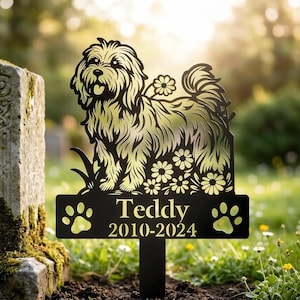 Puede incluir: Estaca conmemorativa para mascotas de metal negro con un diseño recortado de un perro con flores. El nombre "Teddy" y las fechas "2010-2024" se muestran en una placa rectangular con huellas de patas. Para jardín.