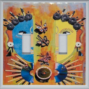 May include: A light switch cover with a colourful abstract design featuring two faces, butterflies, and a sunburst pattern. The design is made with mixed media, including paper, fabric, and other materials. The artist's signature, "Gathinja", is visible in the bottom right corner.