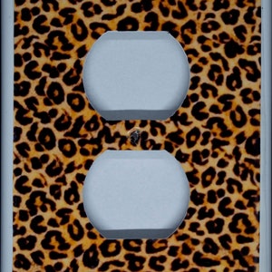 May include: A white electrical outlet cover with a leopard print design. The cover has two standard outlets.