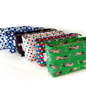 Puede incluir: Una colección de seis pequeñas bolsas rectangulares con cremallera. Las bolsas presentan varios diseños, incluyendo lunares, diseños florales y una tela verde con ilustraciones de perros. Cada bolsa tiene una cremallera marrón y una pequeña etiqueta.