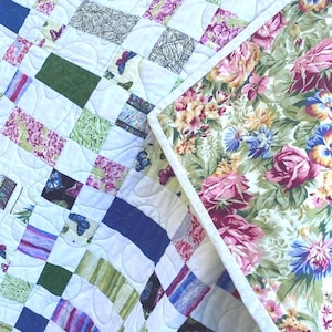 May include: A handmade quilt with a patchwork design. The quilt features a variety of patterned squares in shades of blue, green, purple, and white, with butterfly and floral motifs. The reverse side has a floral pattern.