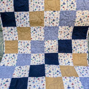 May include: A patchwork quilt featuring a repeating pattern of squares in various colors and designs. The quilt incorporates squares of navy blue, light blue, tan, and white fabric. Some squares have a whimsical print with small figures and trees.