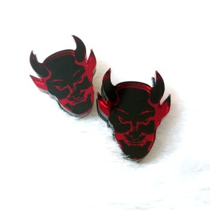 May include: A pair of red and black devil head earrings. The earrings are made of acrylic and have a glossy finish.