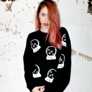 May include: Black sweatshirt with white embroidered snow globes with stars inside. The snow globes are scattered across the front of the sweatshirt.