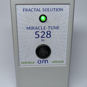 Puede incluir: Un dispositivo rectangular gris con el texto "FRACTAL SOLUTION" y "MIRACLE-TUNE 528 Hz." Tiene una luz verde y un interruptor negro. La parte inferior del dispositivo dice "BIOFIELD Om ORGONE."