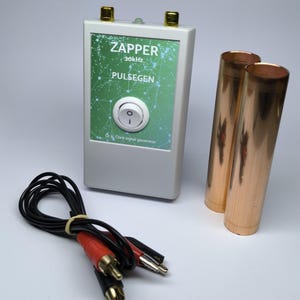 Puede incluir: Un dispositivo electrónico blanco con la etiqueta "ZAPPER 30kHz PULSEGEN", un gráfico verde, un interruptor blanco y dos terminales dorados. También hay dos cilindros de cobre y un cable negro con conectores rojos y negros.
