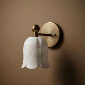 May include: A wall-mounted light fixture featuring a white marble tulip-shaped shade. The fixture has a brass-colored circular backplate and a brass arm. The light is designed to be mounted on a wall.