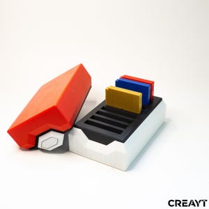 May include: A red, white, and black game cartridge holder with a matching lid. The holder contains three game cartridges in yellow, blue, and red. The design is geometric and modern.