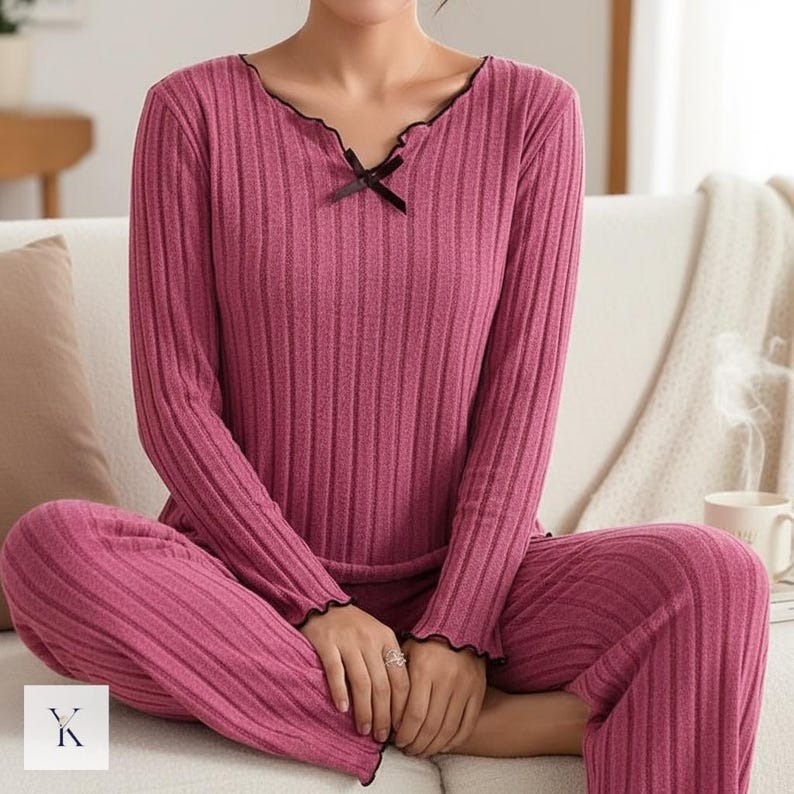 Może przedstawiać: Dwuczęściowy zestaw piżamy z dzianiny prążkowanej w głębokim r&oacute;żowym kolorze. Top z długim rękawem ma falisty dekolt z czarnym wykończeniem i małą kokardką. Spodnie są pełnej długości. Zestaw został zaprojektowany z myślą o komforcie i relaksie.