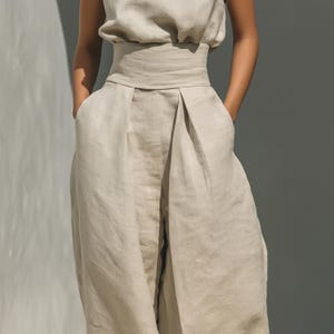 Peut inclure: Un pantalon taille haute beige dot&eacute; d'une large ceinture structur&eacute;e et de plis profonds sur le devant, cr&eacute;ant une silhouette volumineuse et d&eacute;contract&eacute;e. Le v&ecirc;tement est confectionn&eacute; dans un tissu textur&eacute; de couleur beige naturel.