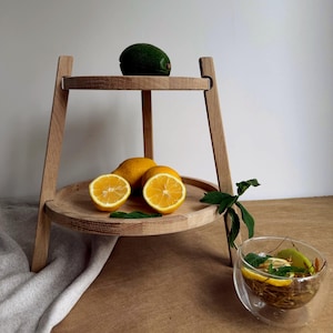 Könnte beinhalten: Ein zweistufiges Serviertablett aus Holz mit natürlichem Finish. Die obere Ebene enthält eine grüne Avocado, während die untere Ebene ganze und halbierte Zitronen zeigt. Ein Glas Tee mit Zitrone und Minze steht in der Nähe.