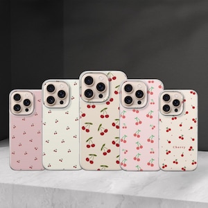 Puede incluir: Cinco fundas para teléfono con diseños de cerezas. Las fundas tienen fondos rosas y crema, con patrones de cerezas rojas. La funda de la derecha tiene la palabra "Cherry" impresa.