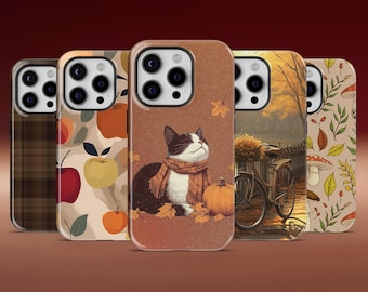 May include: Five phone cases with autumn-themed designs. One case features a black and white cat wearing a scarf, with a pumpkin and leaves. Other cases have apple, plaid, bicycle, and mushroom patterns. The cases are on a brown background.