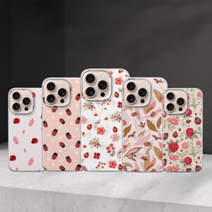 May include: A collection of five phone cases with various floral and ladybug patterns. The cases feature a range of designs, including red ladybugs on a pink background, floral arrangements, and leaf patterns. The cases are displayed on a white surface.