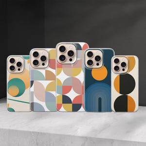 Op de afbeelding: Vijf telefoonhoesjes met kleurrijke geometrische ontwerpen. De hoesjes hebben verschillende patronen, waaronder cirkels, bogen en abstracte vormen in tinten blauw, oranje, geel en groen. De hoesjes worden op een wit oppervlak weergegeven.
