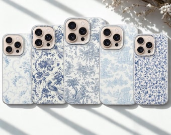 Op de afbeelding: Vijf smartphonehoesjes op een rij, elk met een verschillend blauw-wit patroon geïnspireerd op toile de jouy. De ontwerpen bevatten bloemmotieven, vogels en pastorale scènes op een witte achtergrond met goudkleurige uitsparingen voor de camera.