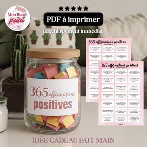 Puede incluir: Un tarro de cristal lleno de cuadrados de papel de colores, etiquetado "365 afirmaciones positivas". El tarro tiene una tapa de madera y está acompañado de dos hojas impresas con afirmaciones. El texto "PDF para imprimir" e "idea de regalo hecha a mano" también es visible.