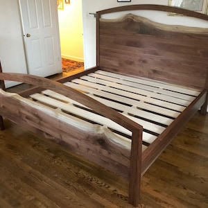 May include: A wooden bed frame with a headboard featuring a live edge design. The headboard is made of walnut wood and has a natural, rustic look. The bed frame is made of solid wood and has a sturdy construction.