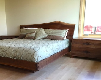 May include: A wooden bed frame with a live edge headboard and a green patterned duvet. The bed is in a bedroom with a wooden nightstand and a bookshelf.