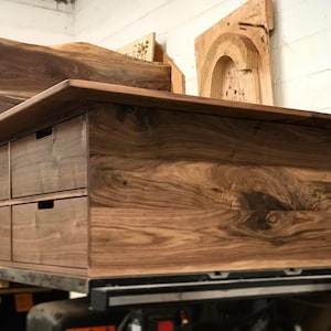 Könnte beinhalten: Eine Kommode aus Holz mit acht Schubladen, aus Walnussholz. Die Kommode hat eine natürliche Holzoptik und steht auf einer Werkbank.