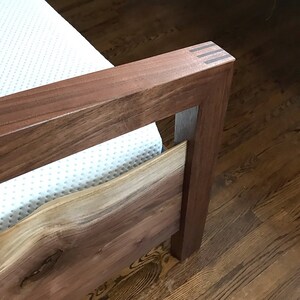 May include: A wooden bed frame with a white mattress. The headboard is made of solid wood with a natural wood finish. The footboard is made of a live edge slab of wood with a natural wood finish.