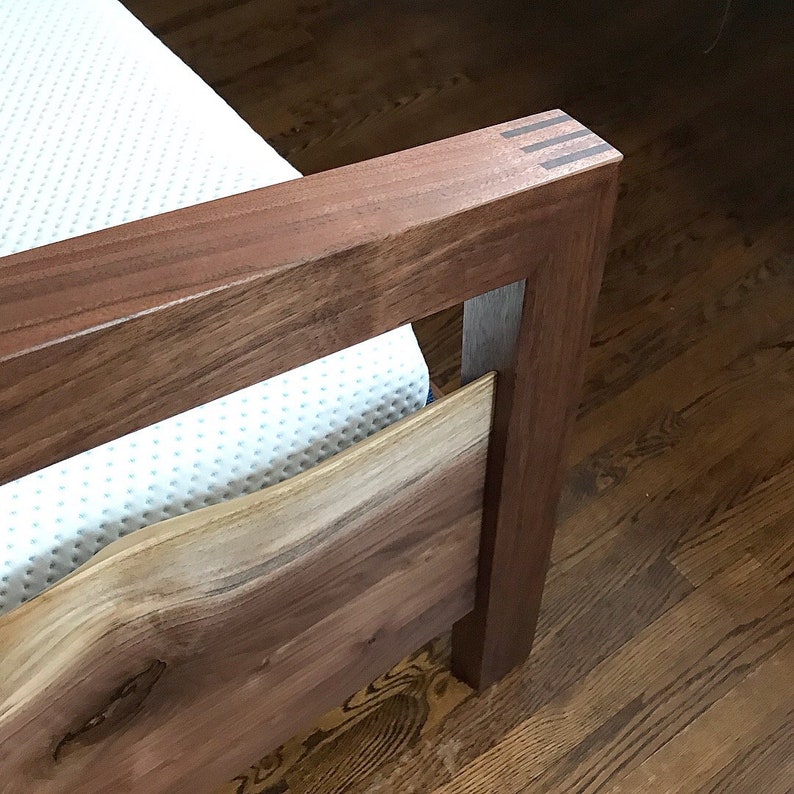 May include: A wooden bed frame with a white mattress. The headboard is made of solid wood with a natural wood finish. The footboard is made of a live edge slab of wood with a natural wood finish.