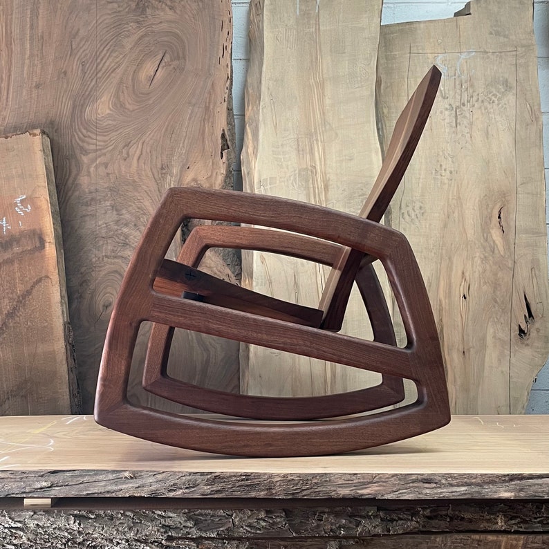 May include: A dark brown wooden rocking chair with a unique, modern design. The chair is made of solid wood and has a smooth, polished finish.