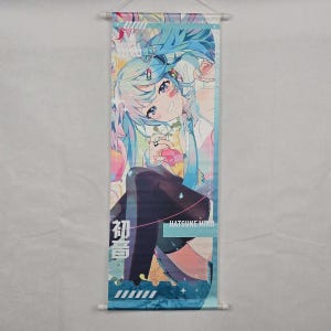 May include: A wall scroll featuring a colorful anime illustration of a character with long, light blue hair. The character is seated and holding a pink object. The text "Hatsune Miku" is visible. The scroll is approximately 24 inches long.