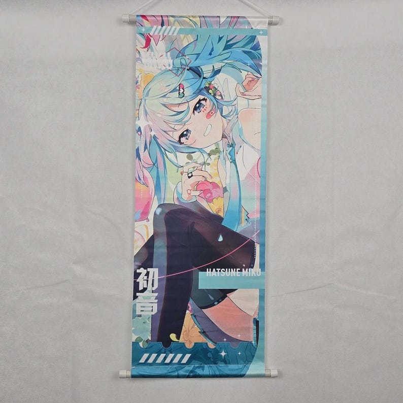 May include: A wall scroll featuring a colorful anime illustration of a character with long, light blue hair. The character is seated and holding a pink object. The text "Hatsune Miku" is visible. The scroll is approximately 24 inches long.