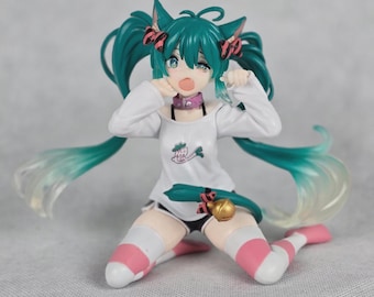 May include: A figurine of a character with teal hair styled in pigtails with cat ears and pink bows. The character wears a white long-sleeved shirt, black shorts, and pink and white striped knee-high socks. A pink collar and a tail with a gold bell are also visible.