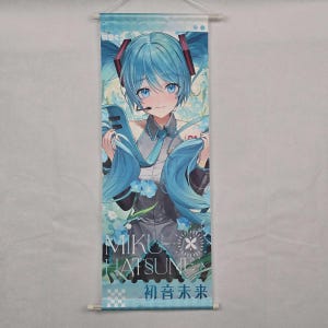 May include: A wall scroll featuring a blue-haired anime character with a microphone headset. The character is wearing a gray and black outfit with a blue tie. The scroll has the text "MIKU HATSUNE" and Japanese characters.