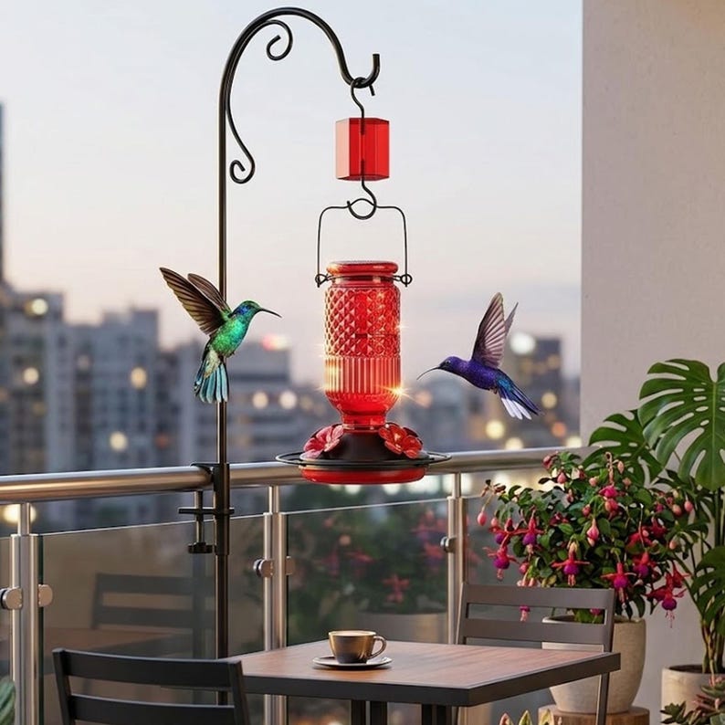 Puede incluir: Un comedero para colibr&iacute;es de vidrio rojo con un patr&oacute;n de diamantes texturizado, suspendido de un gancho de metal negro. El comedero cuenta con una base negra con puertos de alimentaci&oacute;n en forma de flor roja y una tapa hexagonal.