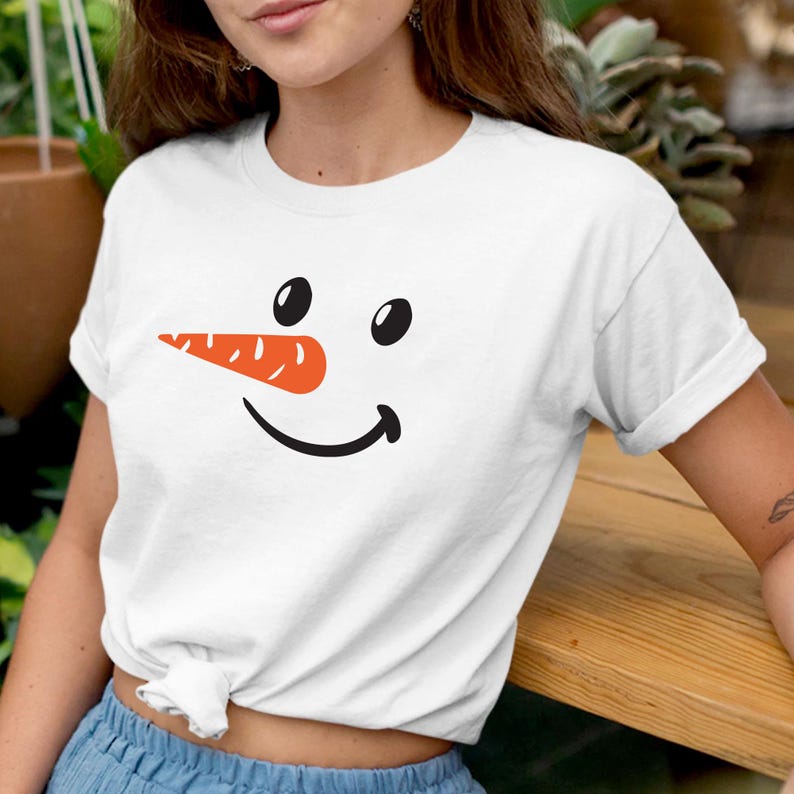 Puede incluir: Camiseta blanca con un dise&ntilde;o de cara de mu&ntilde;eco de nieve. El dise&ntilde;o incluye ojos ovalados negros, una nariz de zanahoria naranja brillante y una sonrisa negra curvada. La camiseta es de estilo casual y de manga corta.