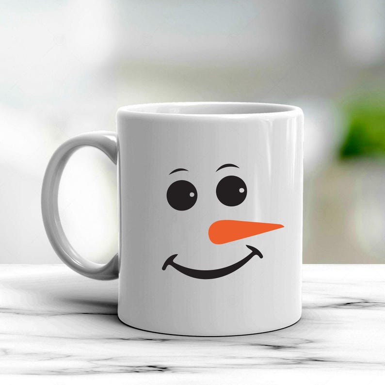 Puede incluir: Taza de cer&aacute;mica blanca con un dise&ntilde;o de cara de mu&ntilde;eco de nieve. El dise&ntilde;o incluye ojos negros, una nariz de zanahoria naranja y una boca sonriente negra. La taza tiene un asa gris y es adecuada para bebidas fr&iacute;as o calientes.