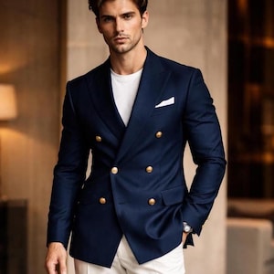 Könnte beinhalten: Ein marineblauer, zweireihiger Blazer mit goldenen Knöpfen, kombiniert mit einem weißen T-Shirt und einer weißen Hose. Der Blazer hat ein Einstecktuch und ist ein klassischer Stil. Eine Uhr am Handgelenk verleiht einen Hauch von Eleganz.