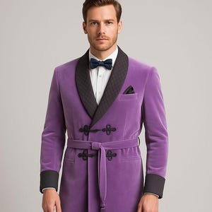 Puede incluir: Una bata de terciopelo morado con cuello chal acolchado negro, puños y pañuelo de bolsillo. La bata presenta un cinturón a juego con borla y cierres de rana decorativos. Se ve una pajarita.