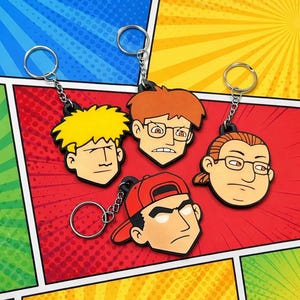 May include: Four rubber keychains featuring cartoon character heads. One has spiky yellow hair, one has orange hair and glasses, one has brown hair in a ponytail with glasses, and one wears a red baseball cap. Each has a silver metal split ring.