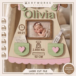 K&ouml;nnte beinhalten: Eine lasergeschnittene Baby-Erinnerungstafel aus Holz in Kleiderform mit dem Namen Olivia, einem Fotorahmen, einer Uhrzeit von 08:21, einem Gewicht von 2,850 kg und einer L&auml;nge von 52 cm. Sie hat zwei gr&uuml;ne Taschen mit rosa Herzen und ein Armband.
