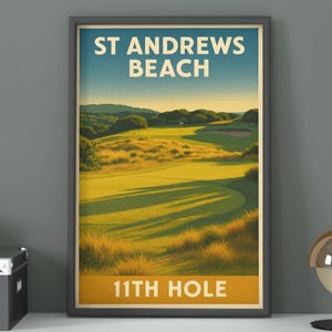 May include: Framed print of St Andrews Beach, featuring a golf course landscape. The artwork has a vintage travel poster style, with text reading "ST ANDREWS BEACH" and "11TH HOLE" in bold letters. The color palette includes greens, blues, and yellows.