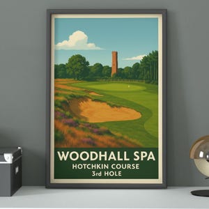 以下が含まれることがあります： 「WOODHALL SPA HOTCHKIN COURSE 3rd HOLE」のテキストが入った、ゴルフコースのシーンの額入りプリント。このアートワークは、緑のゴルフコース、砂のトラップ、青い空の下にある高いレンガの塔を特徴としています。
