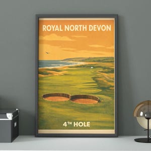 Puede incluir: Póster enmarcado de estilo vintage que representa un campo de golf. El texto "ROYAL NORTH DEVON" y "4TH HOLE" son visibles. La imagen muestra un campo verde, dos búnkeres y una vista costera, con colores cálidos. El marco es gris oscuro.