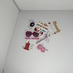 May include: A collection of colorful stickers with various designs and text. Stickers include heart-shaped sunglasses, a burning candle, and phrases like "I'm the problem, it's me" and "Cruel Summer".